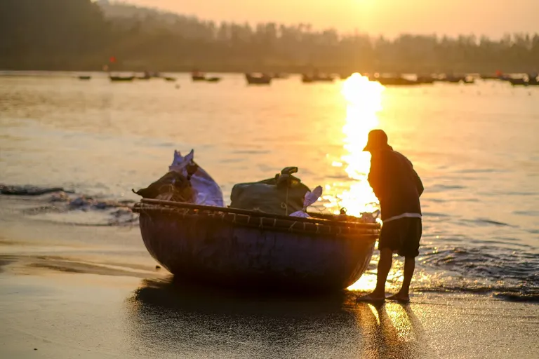A fisherman with a basket boat on the beach at sunrise
