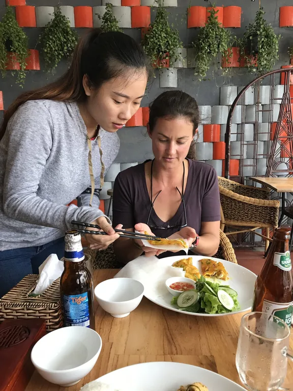 Two friends learning to cook with a local host in a leafy garden kitchen