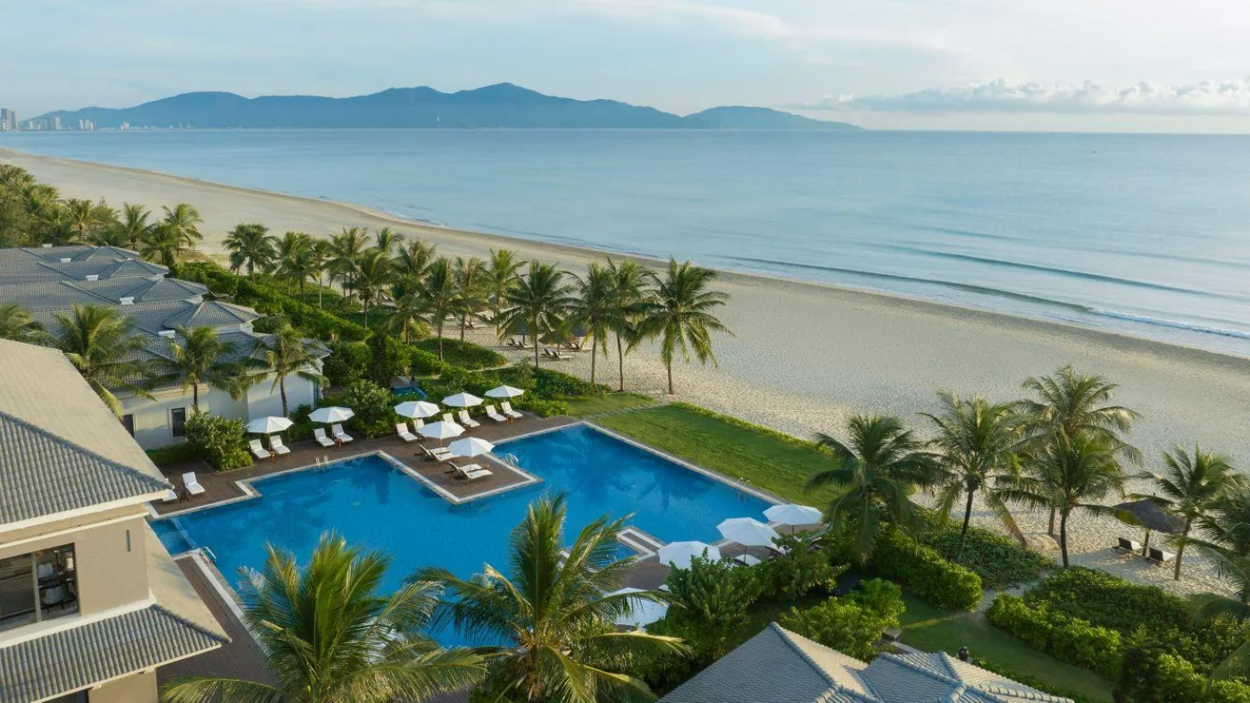 A beachfront resort with palm gardens and a pool above the long sandy shore of Da Nang