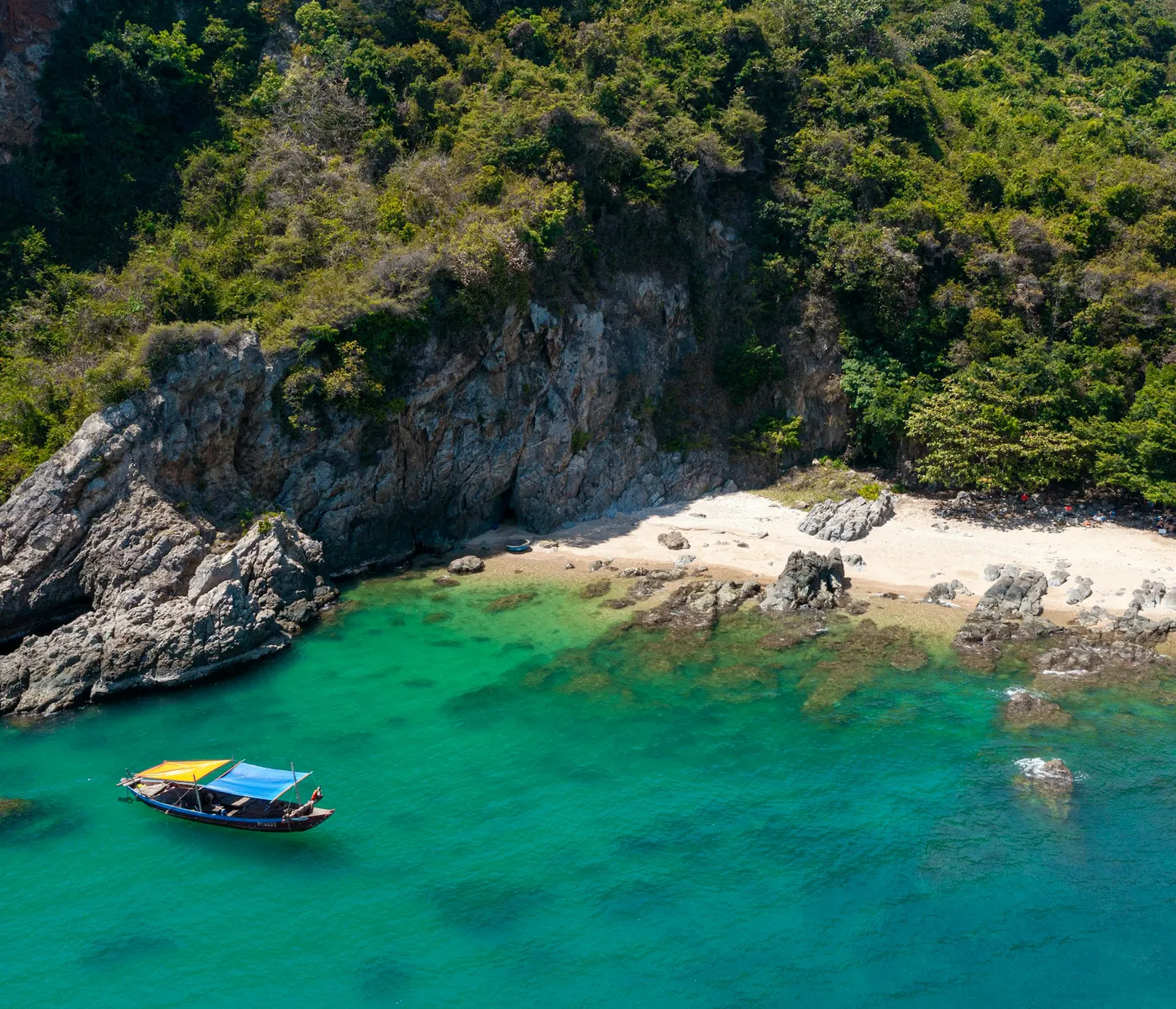 A boat in a turquoise cove below the forested Son Tra cliffs