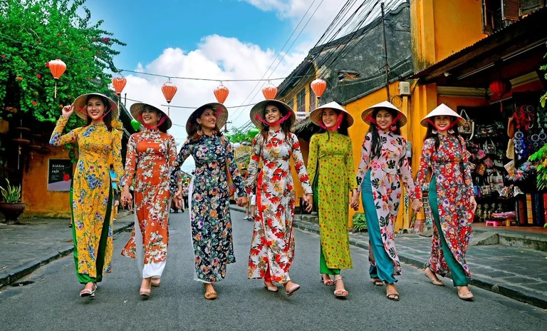 Seven women in floral ao dai and conical hats strolling down a lantern-hung street in Hoi An