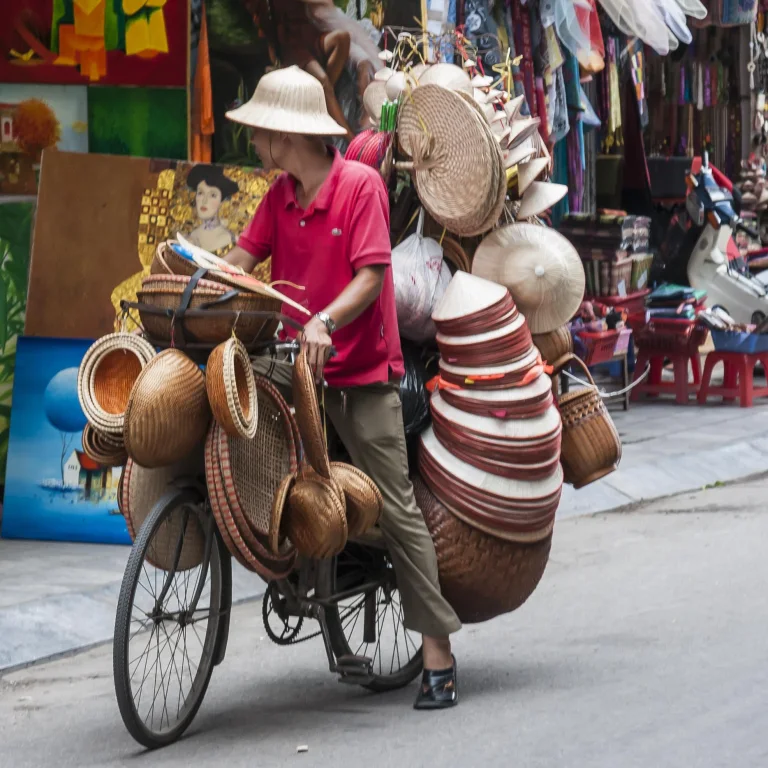 A street vendor wheeling a bicycle piled high with conical hats and baskets in Hoi An