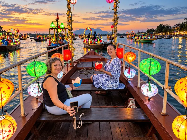 Two friends on a lantern-lit boat on the Hoai River at sunset