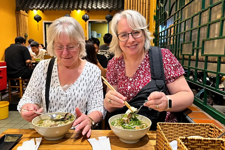 Two friends enjoying bowls of noodle soup in a lantern-lit restaurant