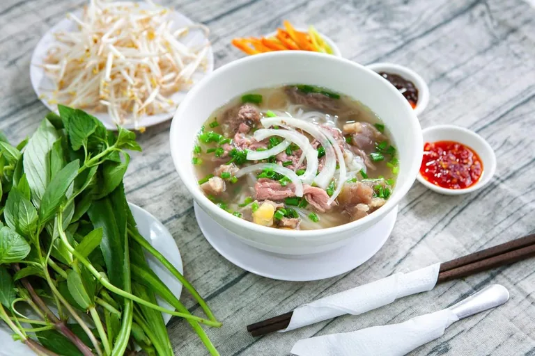 A steaming bowl of pho with fresh herbs and lime