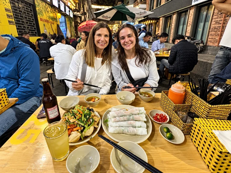 Two friends sharing fresh spring rolls and local dishes at a busy street eatery