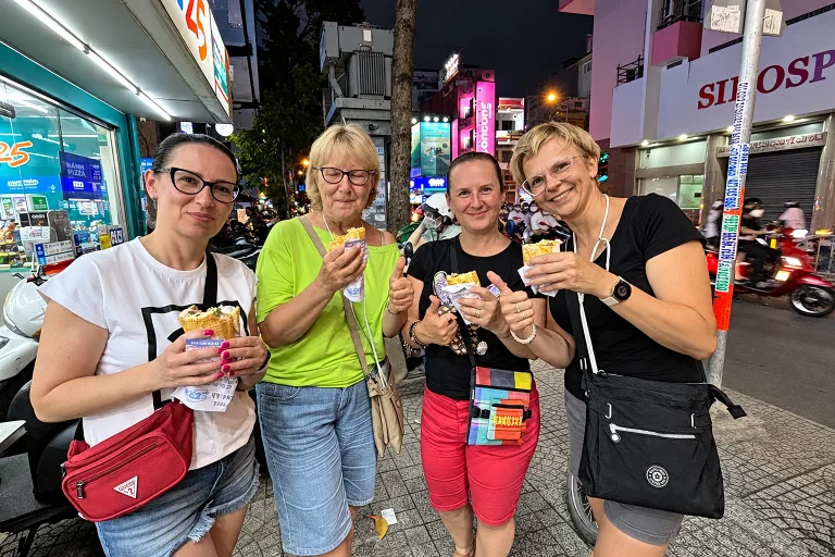 Four friends holding up street snacks on a lively evening street