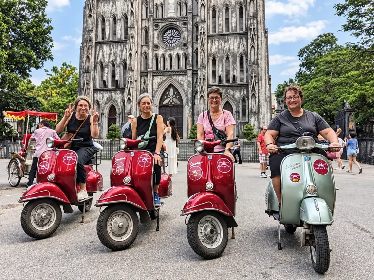 Four women friends posing on vintage Vespas on a sunny city morning