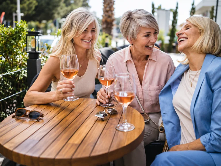 Three women friends laughing over glasses of rosé at a sunny terrace table